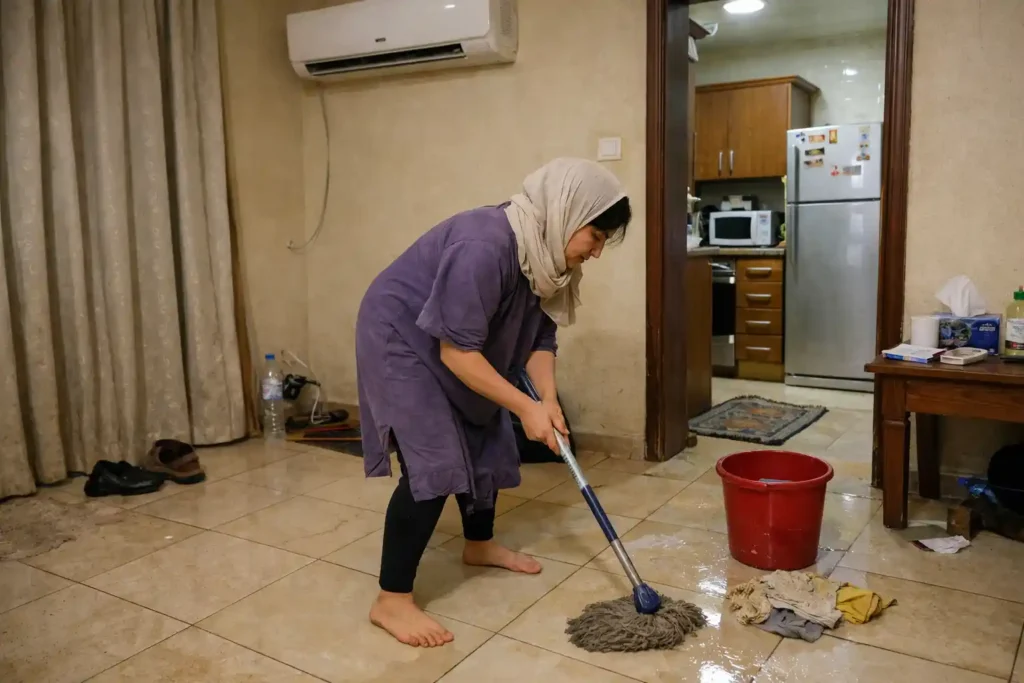 عاملة تنظف أرضية البيت بمساحة معيشة في الرياض، دلو وممسحة وأثر ماء يوضح شغل التنظيف اليومي